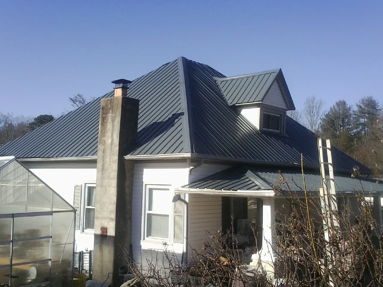 Dark blue standing seam metal roof on a white farmhouse with dormer — Slate & Tile Roof Repair by Roofing Brothers in Iona