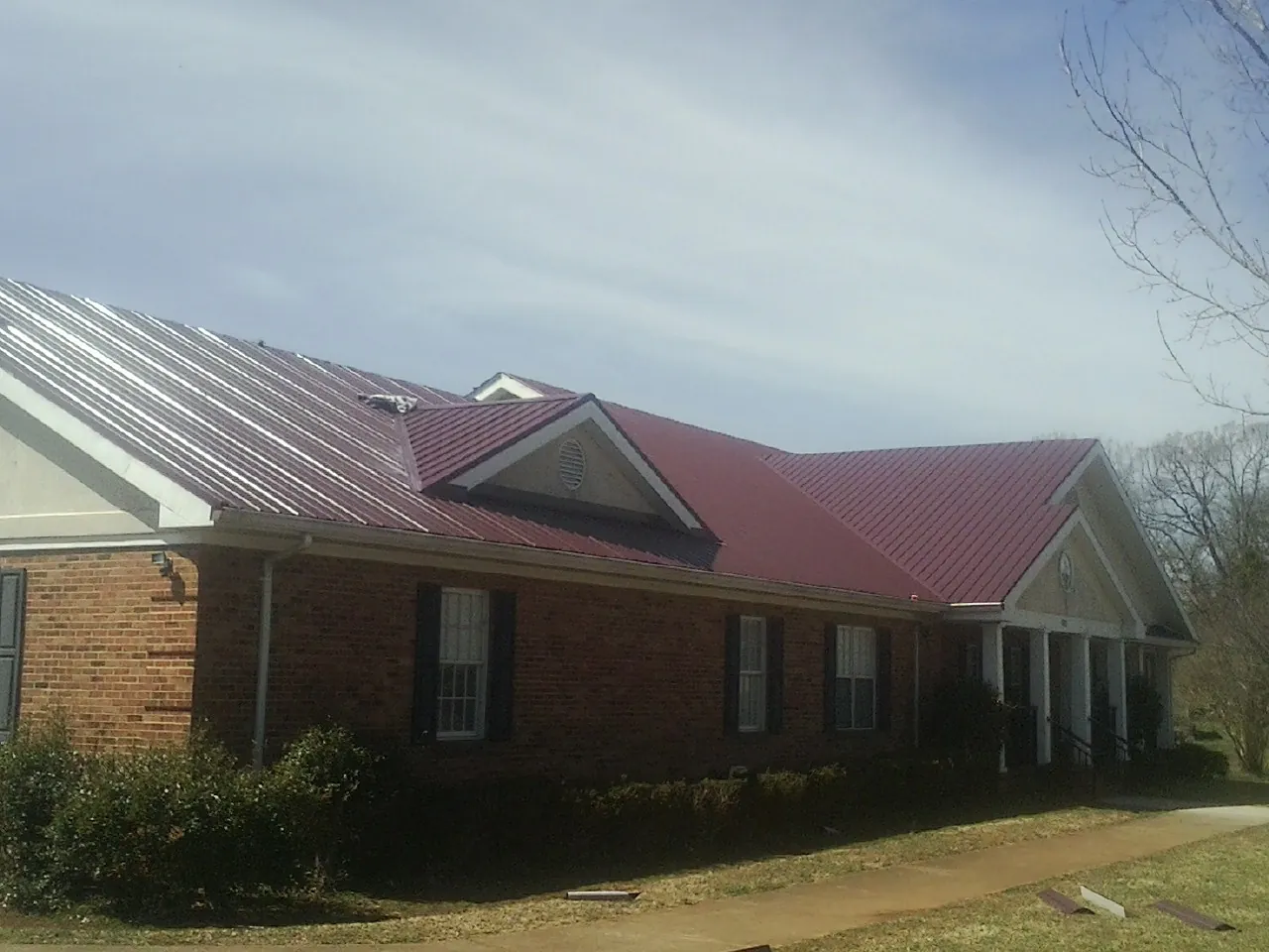 Red metal roof with gabled entries on a long brick building, from a Hail Damage Roof Repair job in Iona