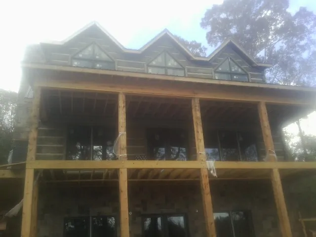 Dormers and porch framing on a large log home under construction — Roof Coating work by our crew in Iona